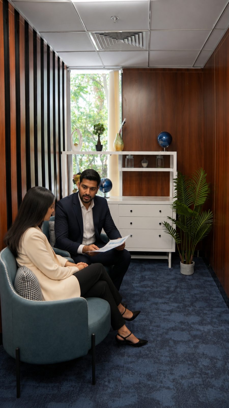 Two people seated in soft armchairs in a private meeting room, reviewing a printed chart together.